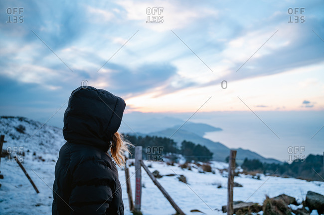 Girl wearing a black down jacket watching the snowy landscape on the coast of Basque Country during winter