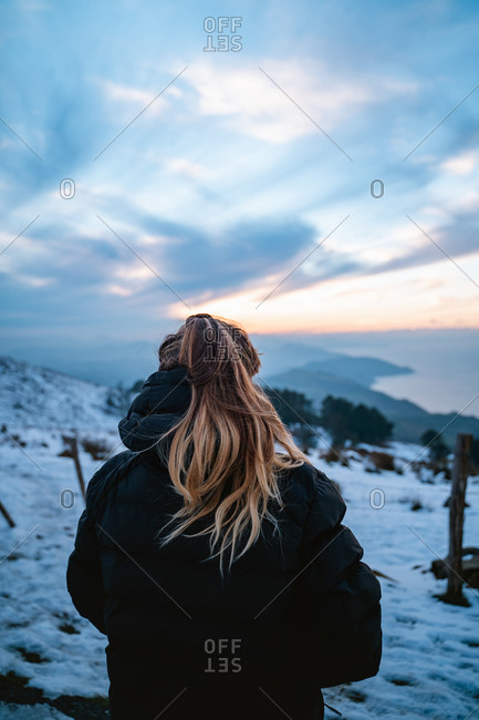 Girl wearing a black down jacket watching the snowy landscape on the coast of Basque Country during winter sunset