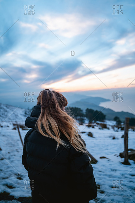 Girl wearing a black down jacket watching the snowy landscape on the coast of Basque Country during winter sunset