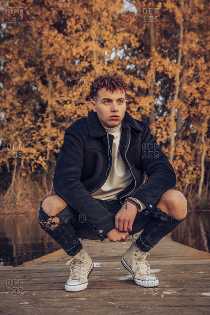 Fashionable young man day dreaming on jetty against autumn tree in forest