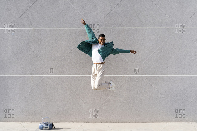 Carefree man jumping with arms outstretched against gray wall