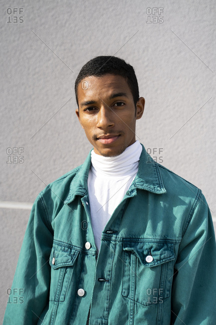 Young man wearing jacket staring while standing against gray wall