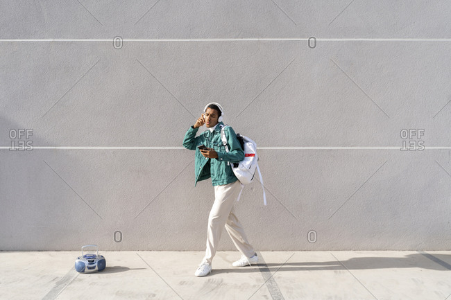 Young man with headphones and mobile phone carrying bag while dancing no footpath