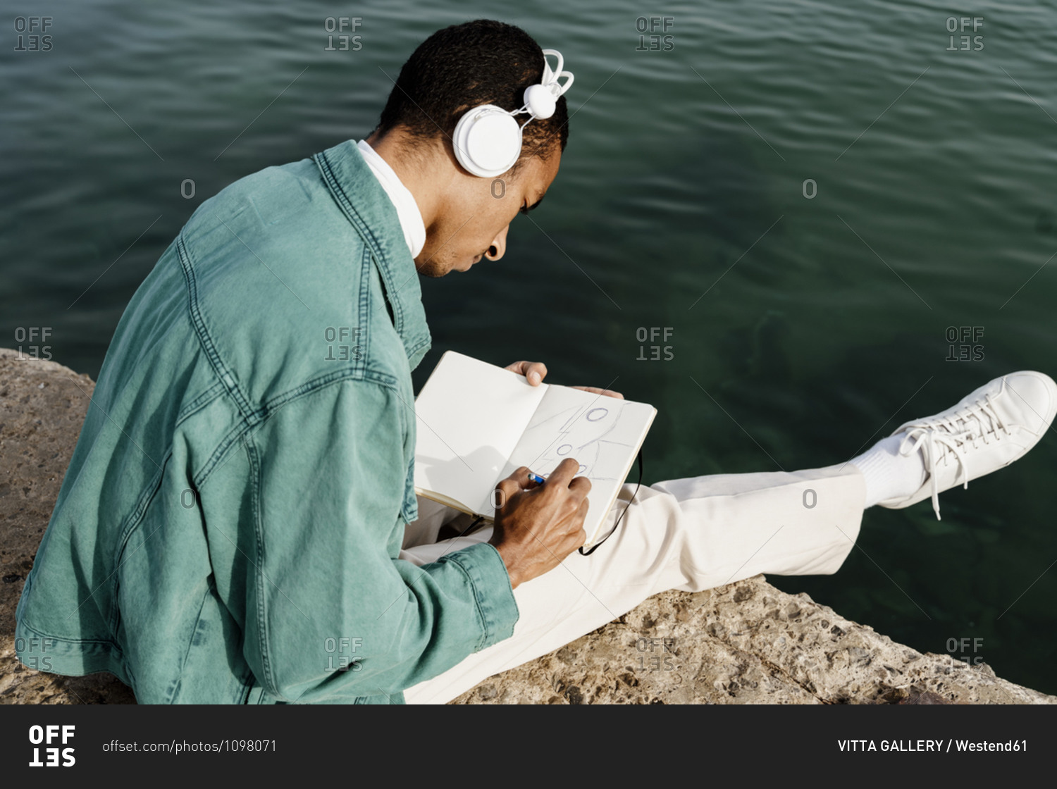 Man drawing in book while sitting on pier by sea
