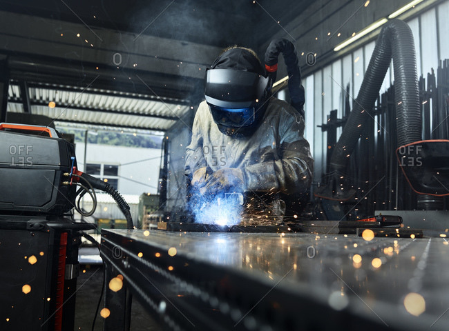 Metal worker wearing protective workwear welding metal while working at factory