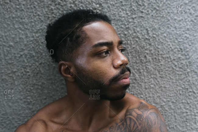 Thoughtful shirtless athlete looking away against gray textured wall