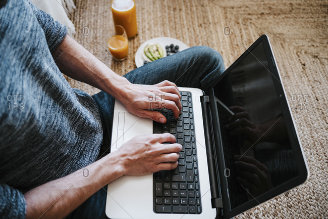 Man using laptop while sitting on floor by breakfast at home