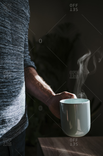 Man holding hot cup of coffee while standing at home