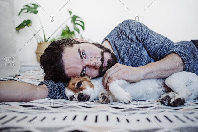 Young man lying with dog on bed at home