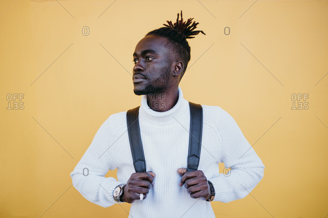 Young businessman with backpack day dreaming against yellow wall