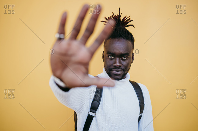 Young man showing hand against yellow background