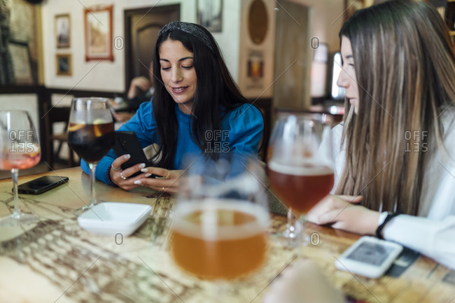 Woman using mobile phone sitting by female friend at restaurant