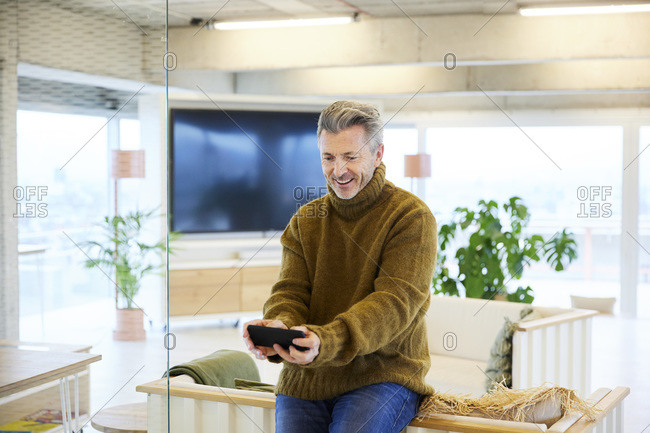 Smiling man playing game on mobile phone while sitting at home