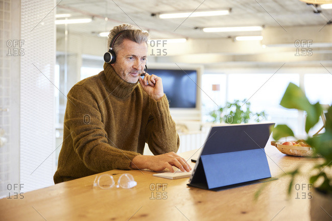 Businessman wearing headset using digital tablet while sitting at office