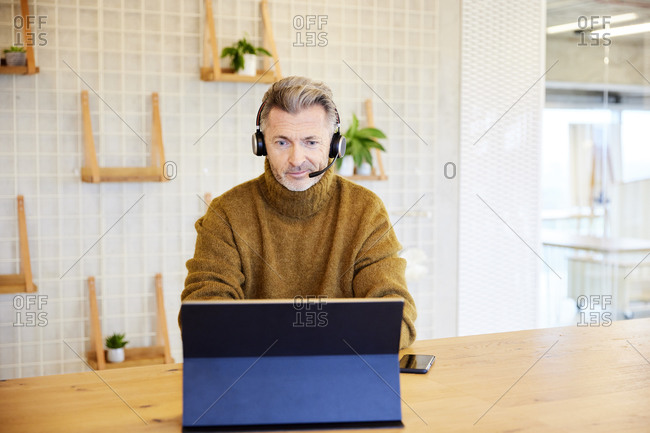 Male businessman wearing headset working on digital tablet while sitting at office