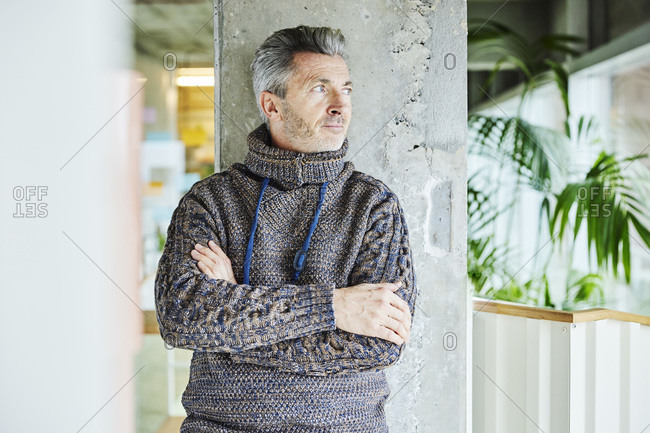 Man wearing turtleneck sweater leaning with arms crossed on pillar at office