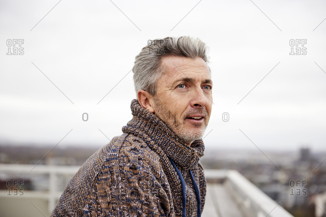 Mature man looking away while standing against sky at rooftop