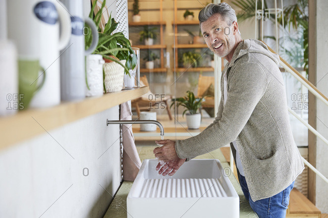 Smiling mature man washing hands while standing by sink at home