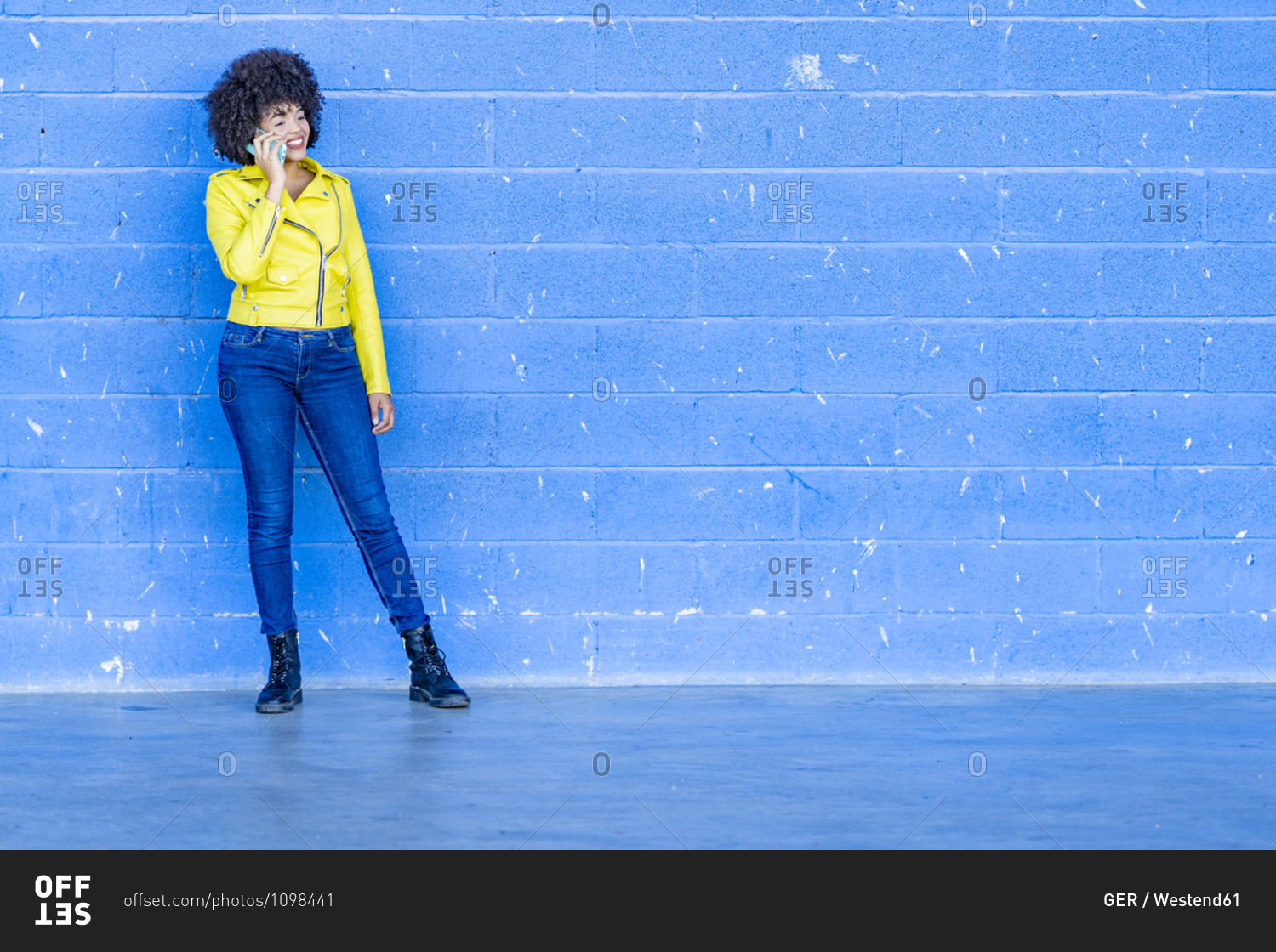 Smiling fashionable young woman talking on mobile phone against blue wall