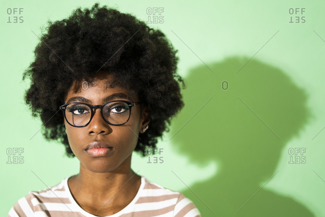 Woman wearing eyeglasses staring while standing against green background