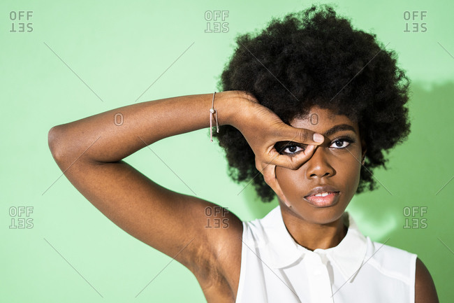 Woman looking through finger frame while standing against green background
