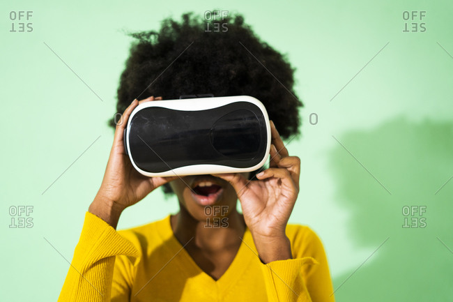 Woman with mouth open using virtual reality headset while standing against green background