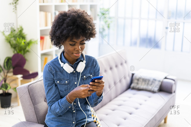 Woman with headphones using mobile phone while sitting on sofa at home