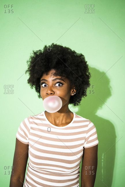 Young woman staring while blowing bubble gum standing against green background