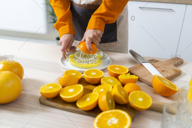 Woman squeezing orange on juicer while preparing juice standing in kitchen at home