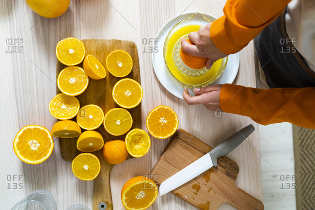 Woman preparing orange juice on juicer while standing by table at home