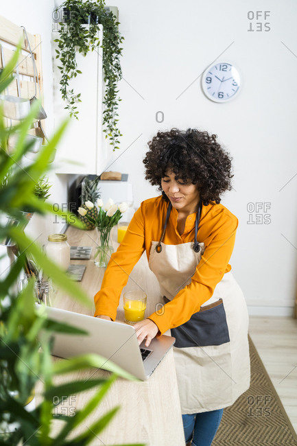 Young woman with orange juice using laptop while standing at home
