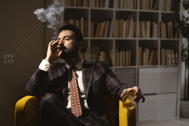Portrait of bearded man enjoying cigar and glass of whiskey