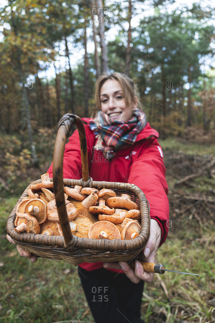Smiling woman showing basket full of mushrooms in forest in autumn