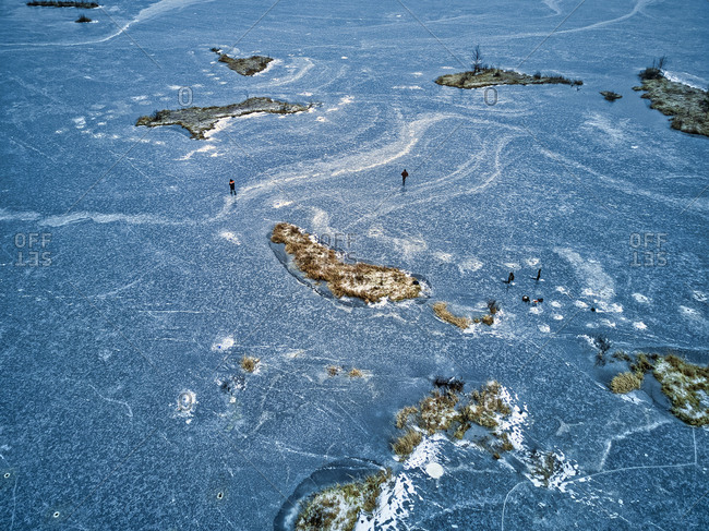 Aerial view of two fishermen walking on surface of frozen lake