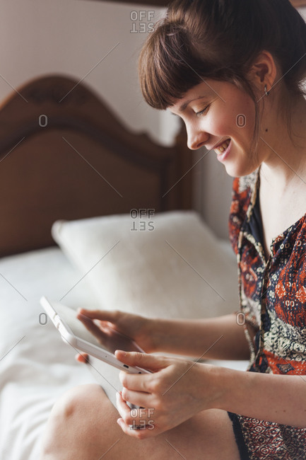 Smiling woman watching video on digital tablet while sitting on bed