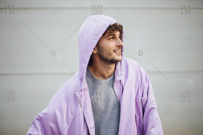 Thoughtful smiling man in violet jacket looking away against gray wall