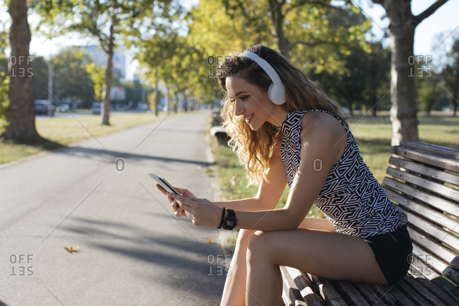 Smiling young woman using digital tablet while listening music in public park on sunny day