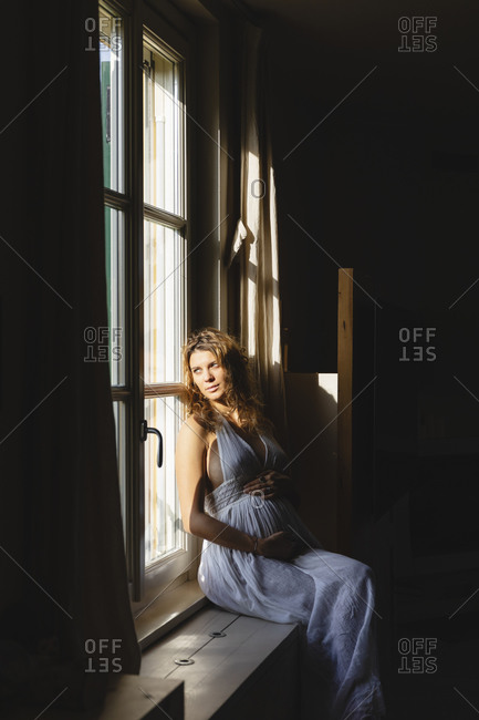 Pregnant woman day dreaming while looking through window in sunlight at home