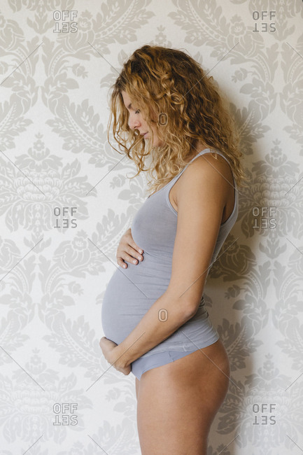 Pregnant woman caring by touching abdomen while standing against wall at home