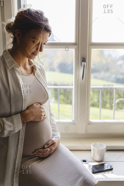 Pregnant woman holding her belly by window