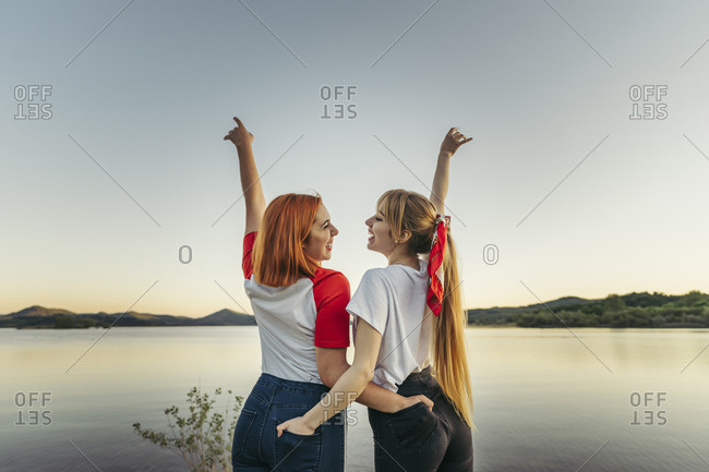 Smiling lesbian couple standing with hands in pockets against clear sky
