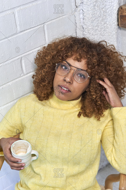 Woman holding coffee cup with hand in hair at cafe