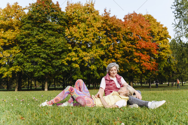 Mature woman lying on female friend's lap on grass at autumn park