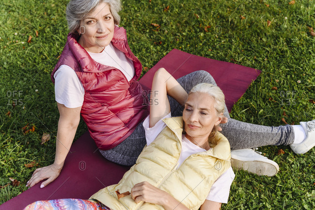 Mature female friends relaxing on grass at public park