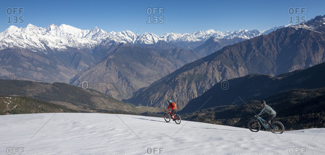 Mountain bikers descend a snow covered slope in the Himalayas with views of the Langtang range in the distance