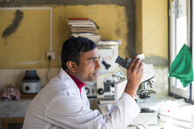 A lab technician working in a laboratory in a small hospital in Nepal holds up a small sample in the light to examine