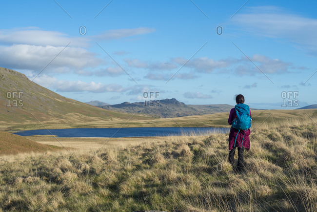 A woman trekking in the English Lake District in Wast Water looks towards Burnmoor Tarn