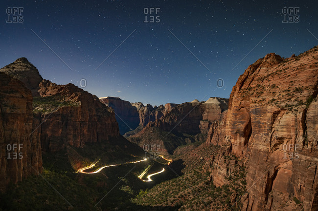 Star filled time sky over Zion Canyon National Park with car headlights making light trails