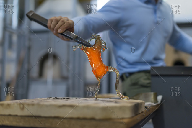 A Murano glass blower holds a red hot glass horse sculpture