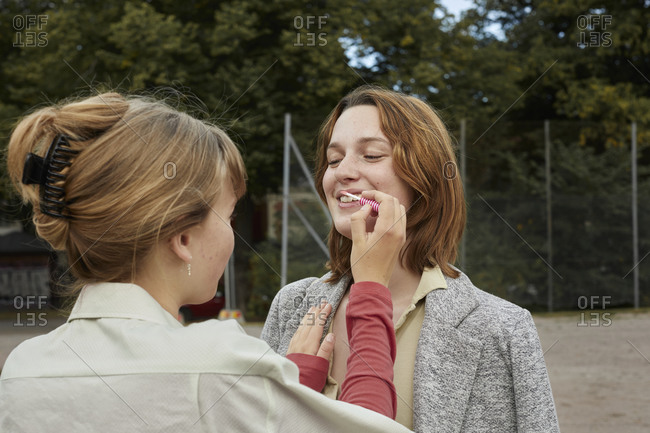 Teenage girl applying lipstick on friends lips